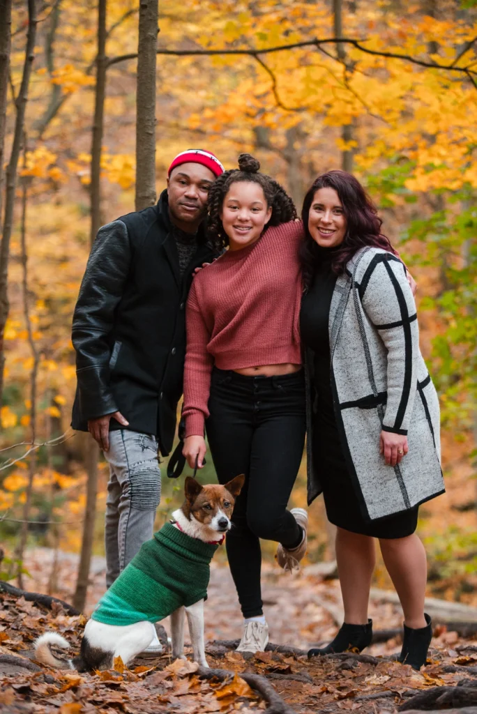 a family of 3 and their dog stand surrounded by autumn leaves - a family portrait shot at Smokey Hollow Falls in Hamilton, Ontario