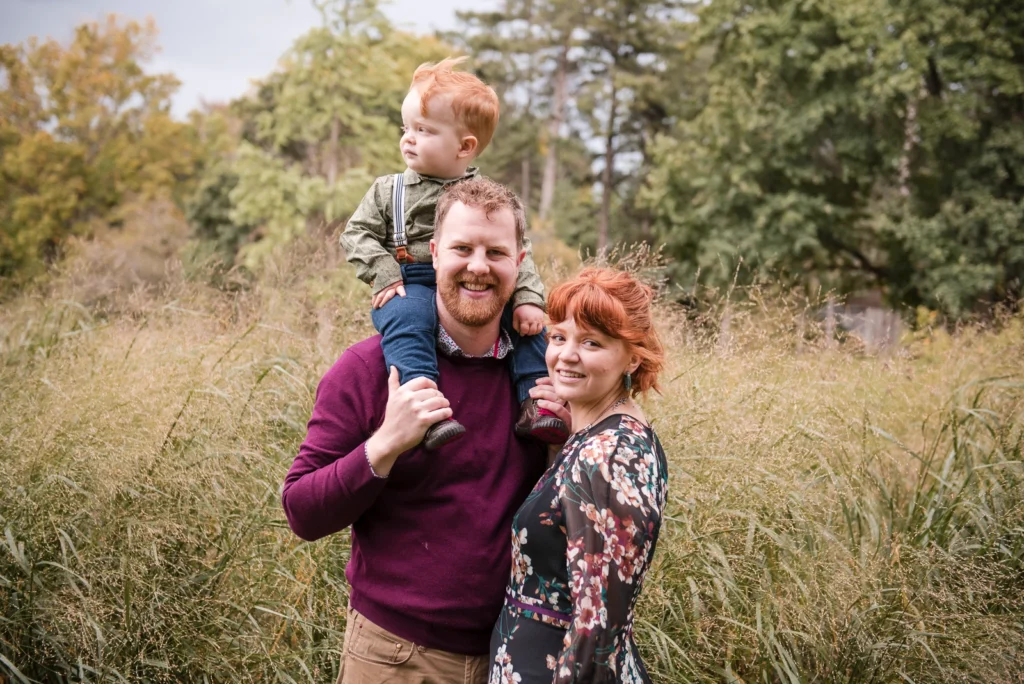 a family stand in a field, the dad holds a young boy on his shoulders - shot at Gage park in Hamilton, Ontario
