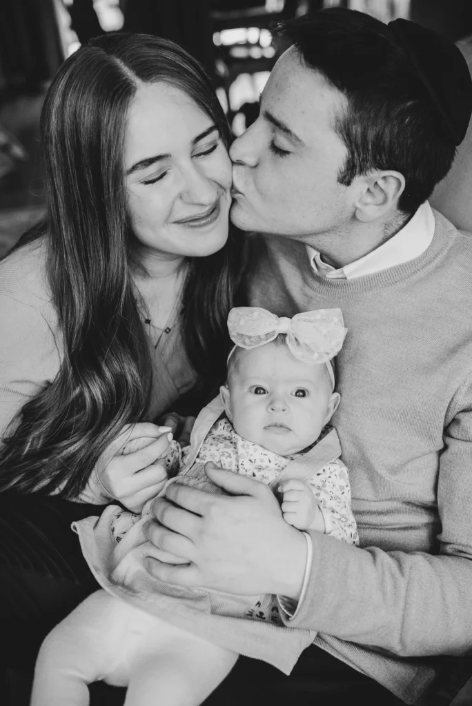 a man kisses his wife and holds his baby. in black and white.