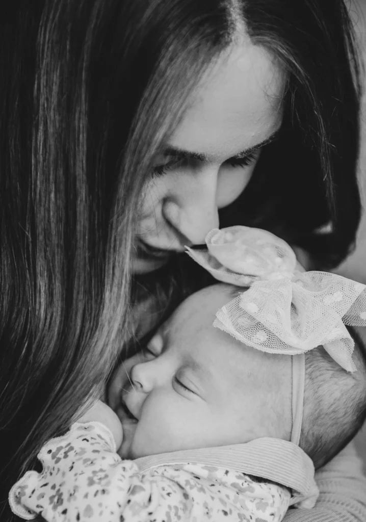 a woman gives her sleeping baby a gentle kiss in black and white