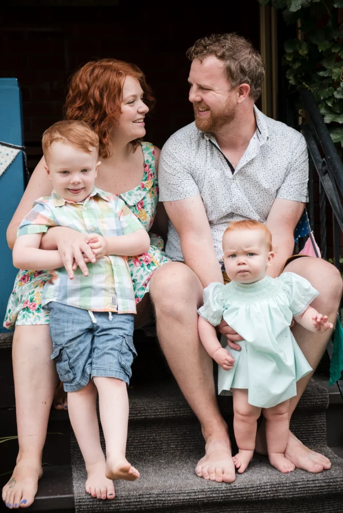 a family of four sit on their front steps