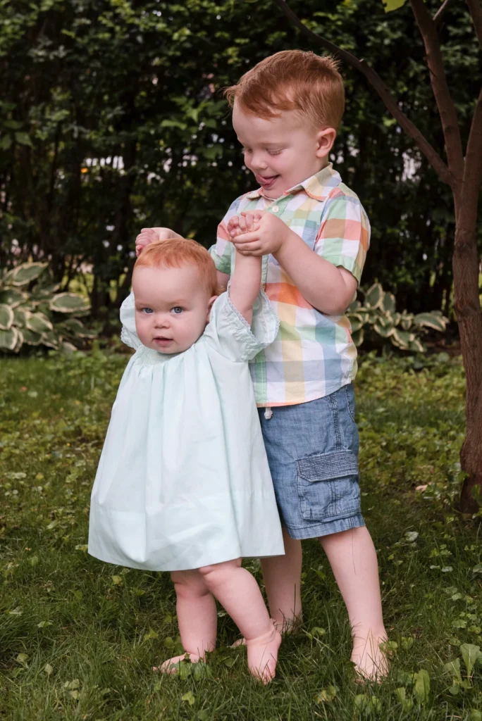 a little boy holds his baby sisters hands to help her walk
