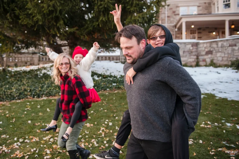 a mother and father race with their son and daughter riding piggy back - a family portrait shot at Paletta Mansion in Burlington, Ontario
