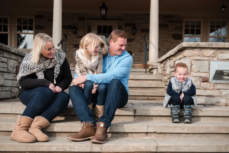 a mother, father and little girl look across at their mischievous little son sitting on the other end of the stairs - a family portrait shot at Paletta Mansion in Burlington, Ontario