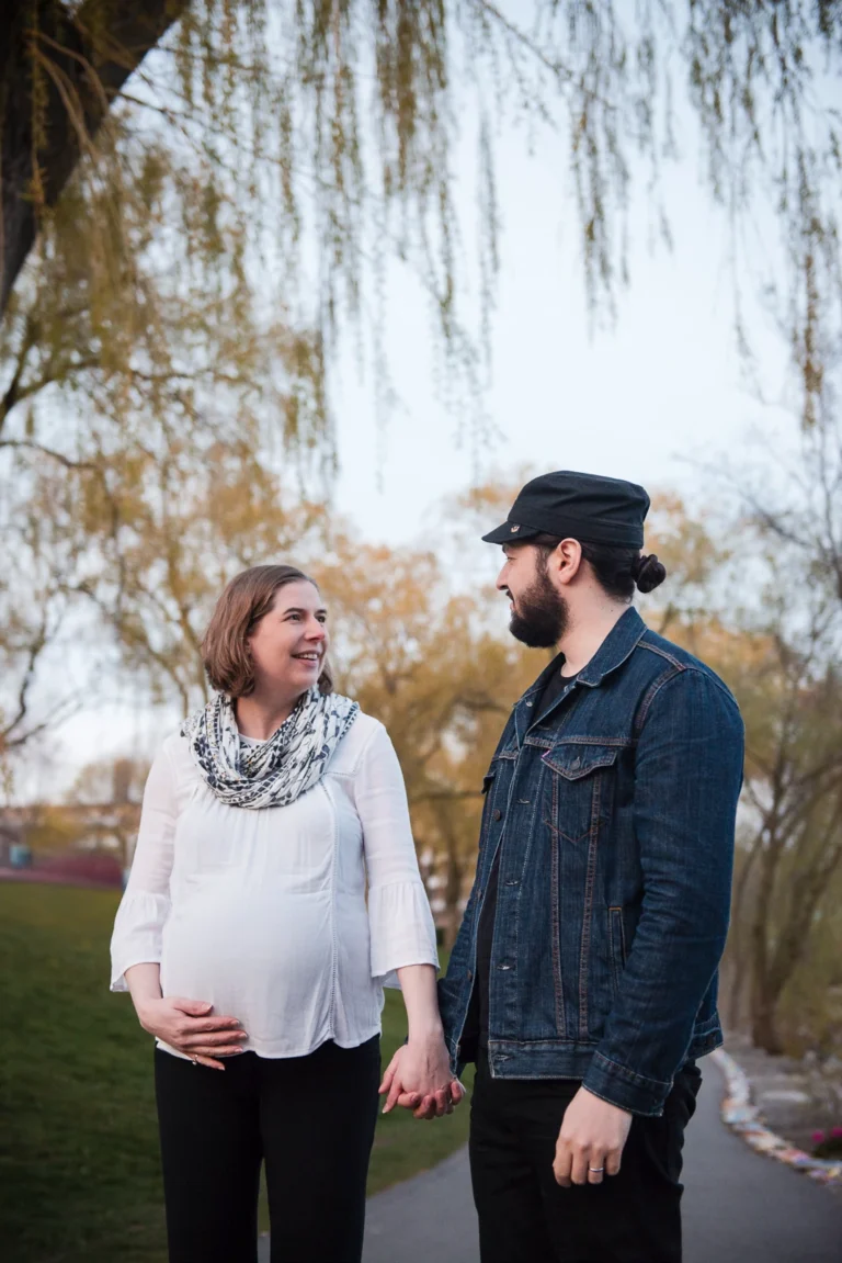 a couple walks in a park as the woman holds her pregnant belly - a family portrait shot in Hamilton, Ontario