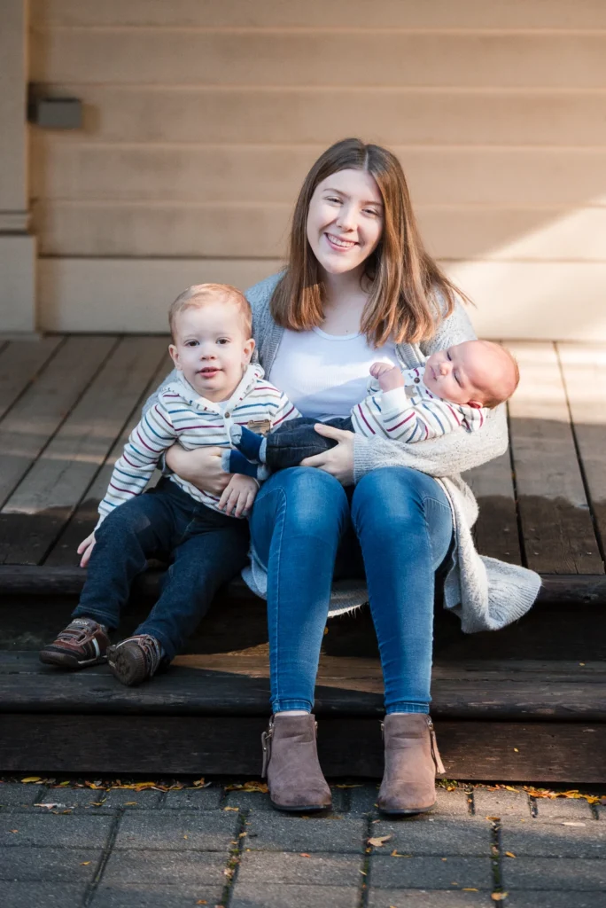 a girl holds her baby sister and her toddler brother while sat on porch stairs - a family portrait shot in battlefield park in Hamilton, Ontario