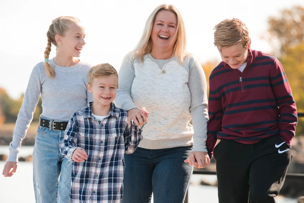a mother walks laughing with her children- a family portrait shot in a personal backyard in stoney creek in Hamilton, Ontario- a family portrait shot in a personal backyard in stoney creek in Hamilton, Ontario