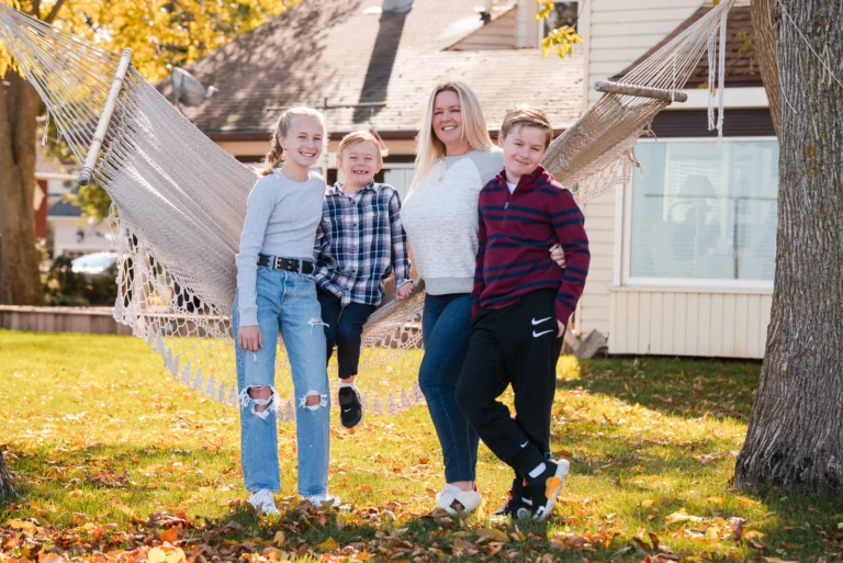 a mother and her three children lean against a hammock in their backyard - a family portrait shot in a personal backyard in stoney creek in Hamilton, Ontario
