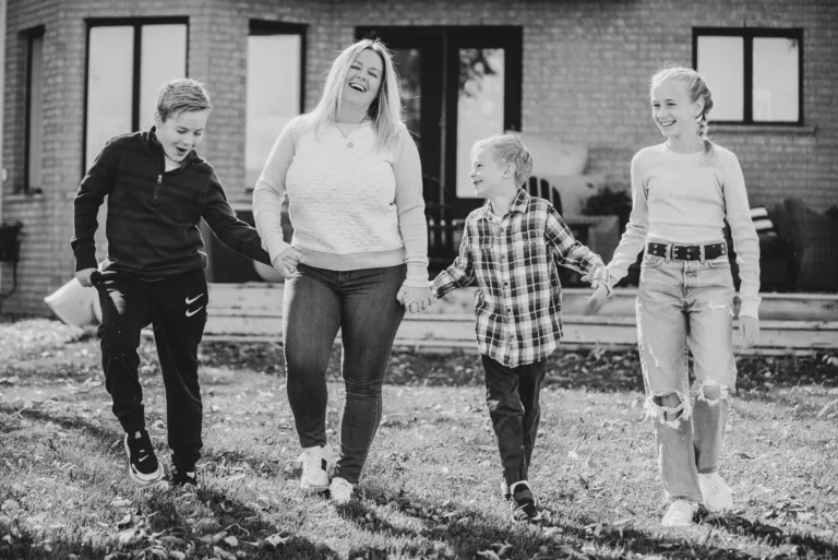 a woman and her three children walk holding hands in their backyard in black and white - a family portrait shot in a personal backyard in stoney creek in Hamilton, Ontario
