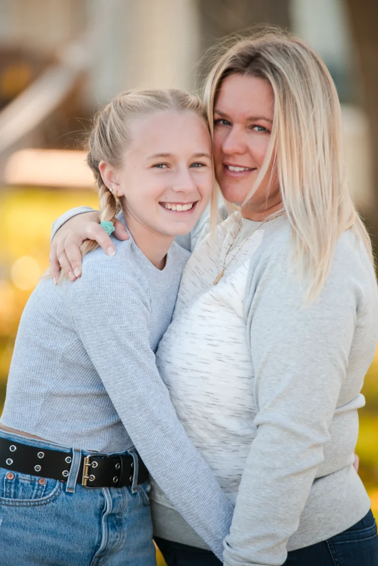 a mother and daughter hug and smile at the camera- a family portrait shot in a personal backyard in stoney creek in Hamilton, Ontario