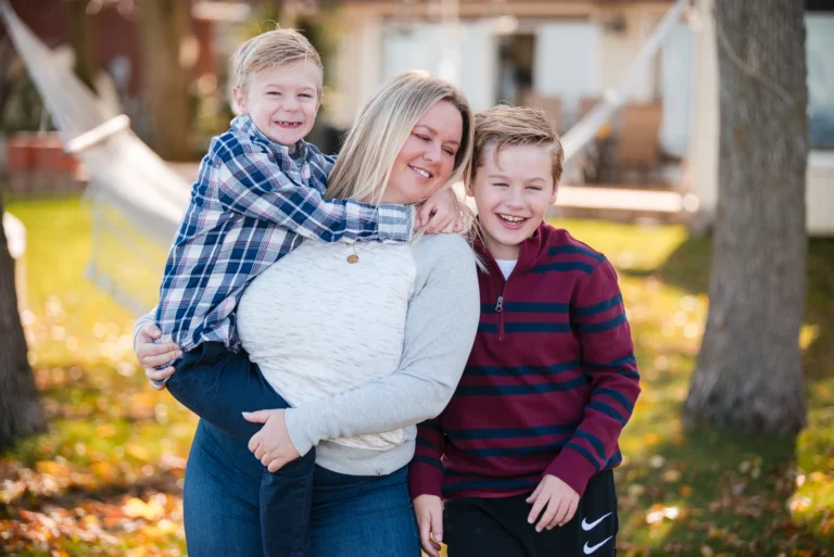 a mother holds her little boy and looks at her other son in their backyard - a family portrait shot in a personal backyard in stoney creek in Hamilton, Ontario