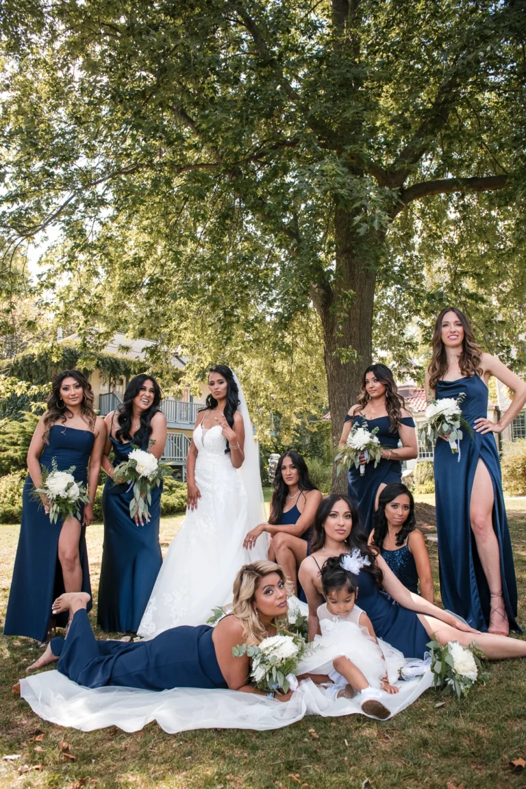 A bride and her bridesmaids playfully gather under a tree. Shot at Adamson Estate by Pixelesque Photography - Hamilton Wedding Photographer.