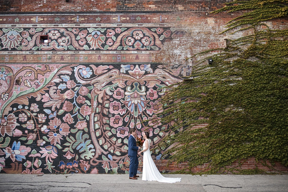 a couple share a moment with each other against a mural. Shot at the carpet factory by Pixelesque Photography - Hamilton Wedding Photographer.