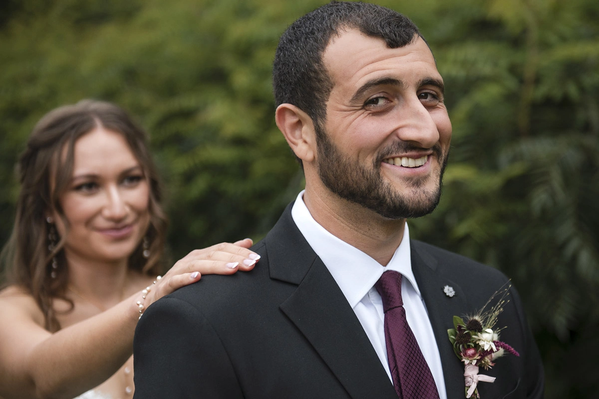 a groom looks at the camera as the bride stands behind him for the first look. Shot by Pixelesque Photography - Hamilton Wedding Photographer.