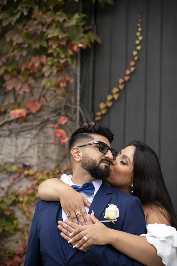 a couple share a kiss in front of a vine covered brick wall - shot at dundurn castle - hamilton wedding venue - shot by hamilton wedding photographer- Pixelesque Photography