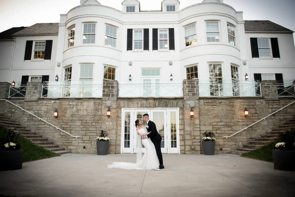 a dip and a kiss from the couple in front of the building. One of many beautiful moments from a wedding at Harding Waterfront Estate in Oakville, by Pixelesque Photography - Hamilton Wedding Photographer.