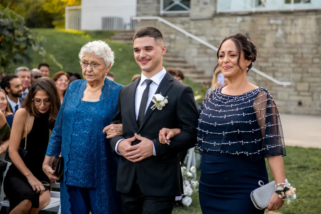 the groom walks down the aisle held by his mother and grandmother. One of many beautiful moments from a wedding at Harding Waterfront Estate in Oakville, by Pixelesque Photography - Hamilton Wedding Photographer.