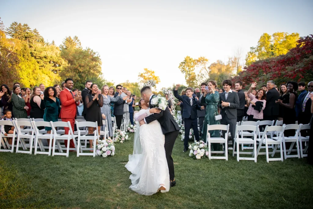 the wedding couple kiss at the exit of the aisle. One of many beautiful moments from a wedding at Harding Waterfront Estate in Oakville, by Pixelesque Photography - Hamilton Wedding Photographer.