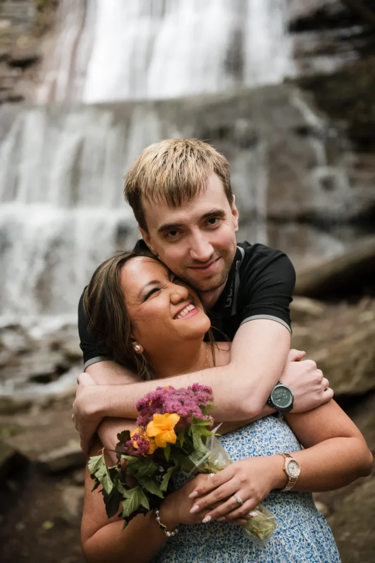 a couple embrace and laugh. A couple stand and look at a raging waterfall. Engagement Session Shot at Sherman Falls, Ancaster, by Pixelesque Photography - Hamilton Wedding Photographer.