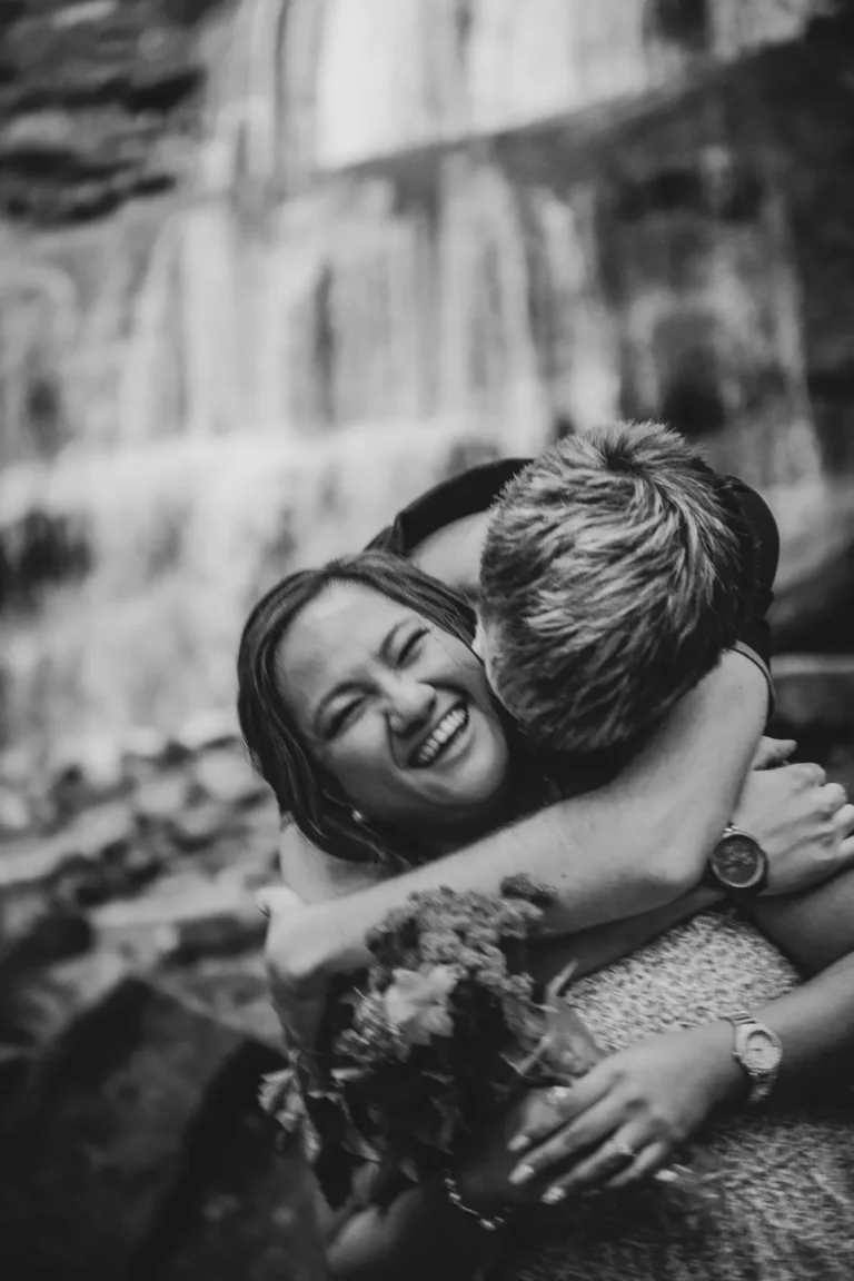 a blurry image of a man nuzzling his partner iwth a waterfall behind them. A couple stand and look at a raging waterfall. Engagement Session Shot at Sherman Falls, Ancaster, by Pixelesque Photography - Hamilton Wedding Photographer.