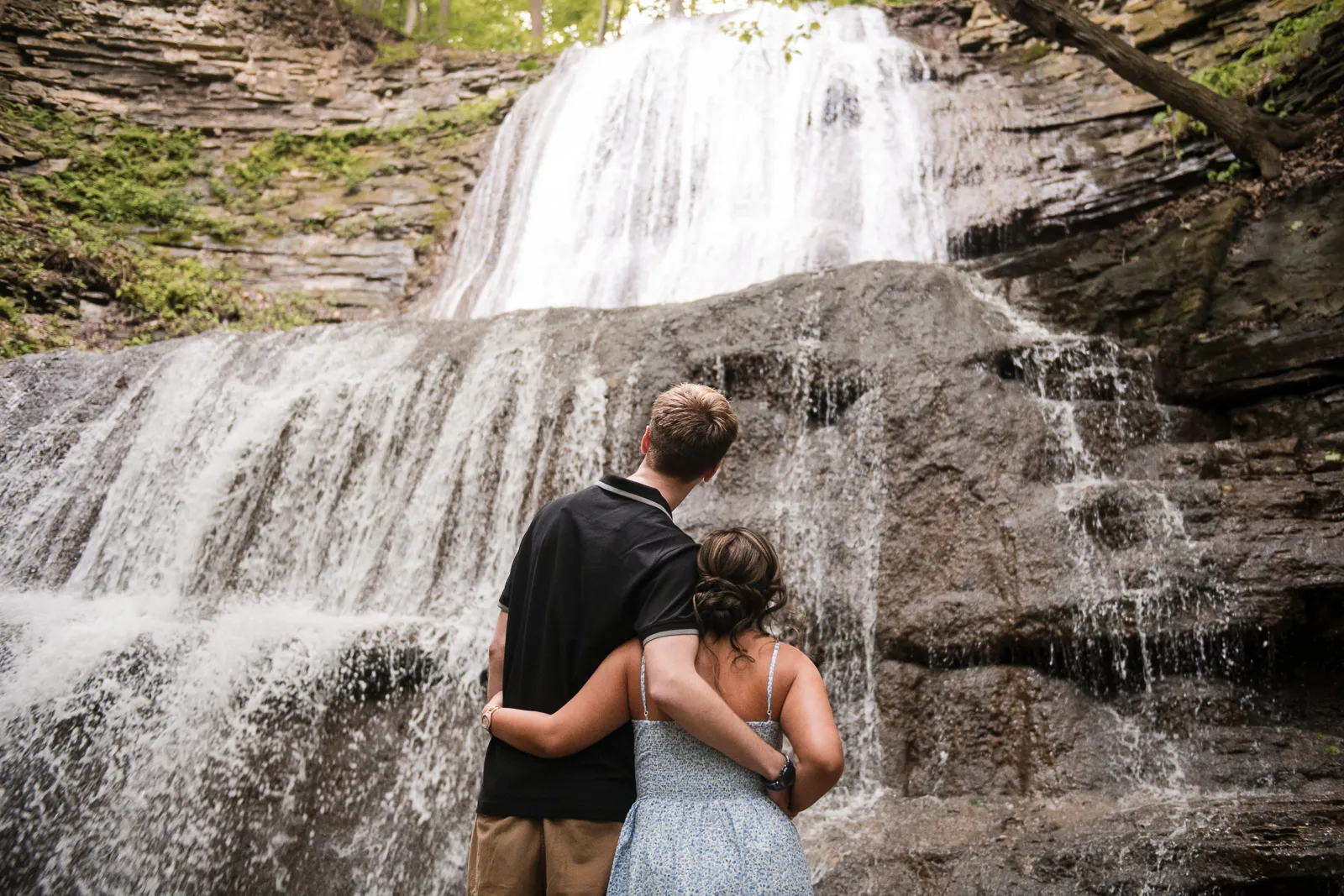 A couple stand and look at a raging waterfall. Engagement Session Shot at Sherman Falls, Ancaster, by Pixelesque Photography - Hamilton Wedding Photographer.