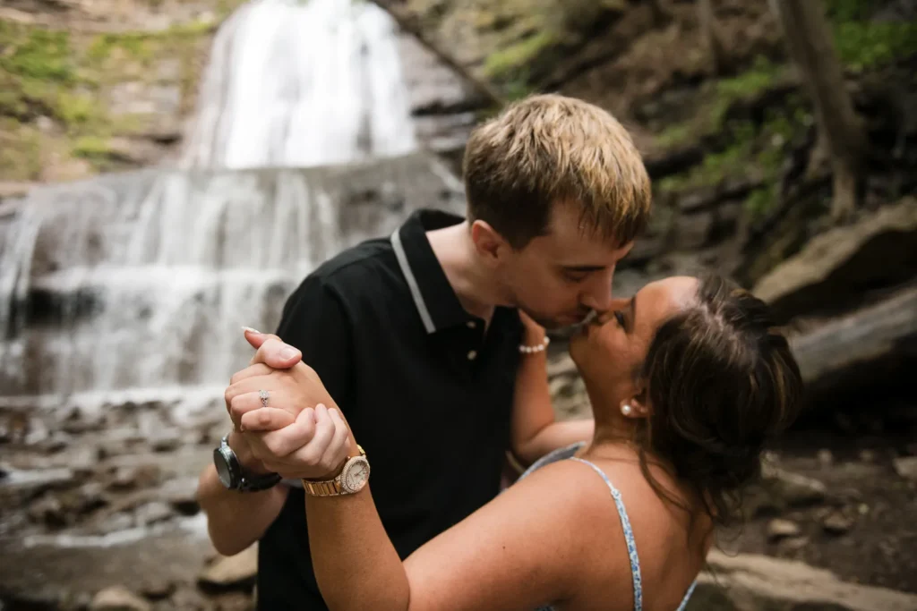 A couple kisses while dancing in front of a waterfall. Engagement Session Shot at Sherman Falls, Ancaster, by Pixelesque Photography - Hamilton Wedding Photographer.