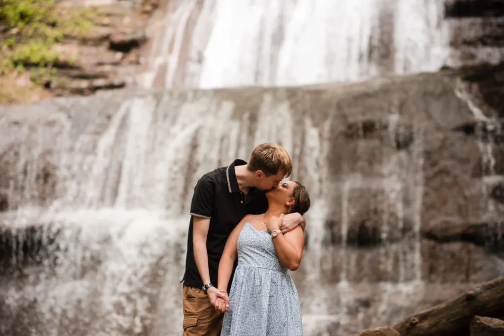 A couple share a kiss in front of a waterfall. Engagement Session Shot at Sherman Falls, Ancaster, by Pixelesque Photography - Hamilton Wedding Photographer.