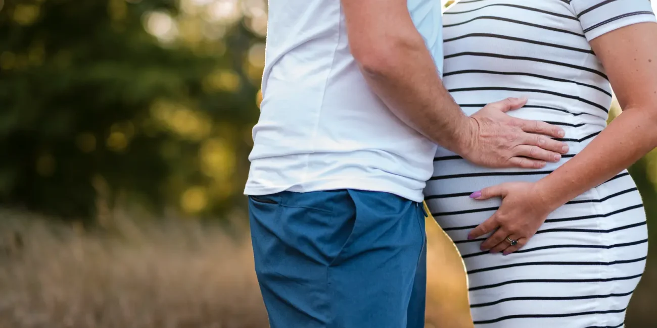 A close up of a pregnant couple sharing an embrace during a maternity shoot at confederations beach park in Hamilton.