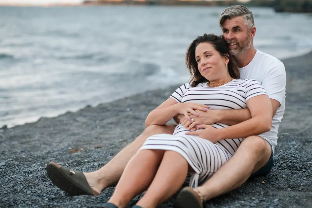 A pregnant couple lay on the beach and look out to the water during a maternity shoot at confederations beach park in Hamilton.