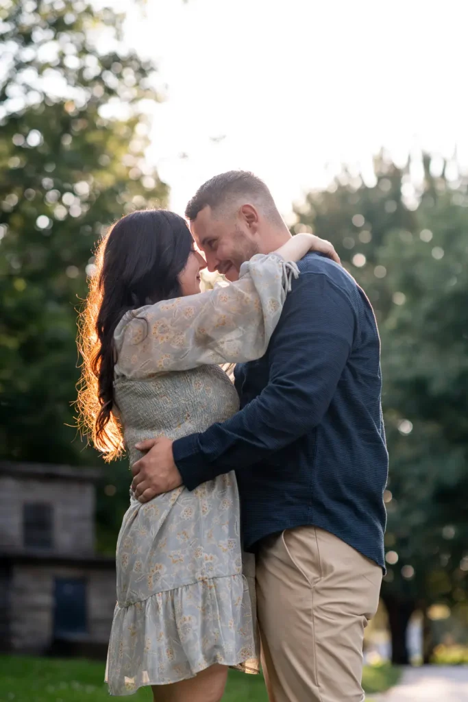 A couple stand head to head with the sun flaring behind them in Simcoe Park. Shot in Niagara-on-the-lake by Pixelesque Photography.