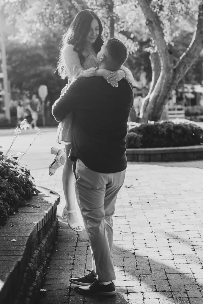 a man picks up his partner as they stare at each other in Simcoe Park. Part of an engagement shoot Shot in Niagara-on-the-lake by Pixelesque Photography.