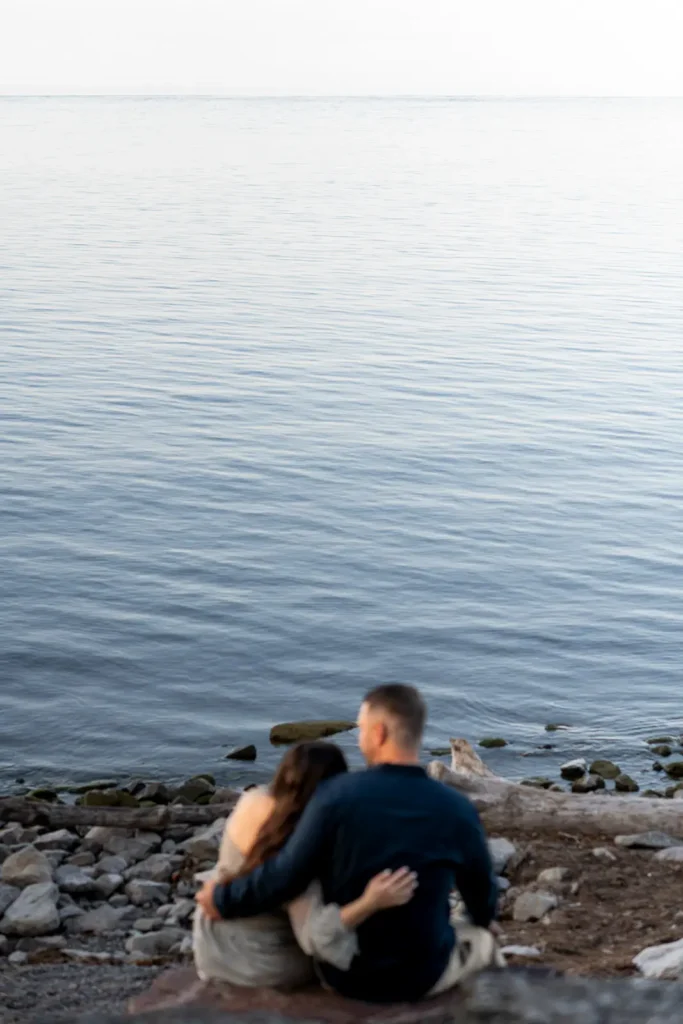 a couple sits on the rocks and looks out to the water at Queen's Royal Park. Part of an engagement shoot Shot in Niagara-on-the-lake by Pixelesque Photography.