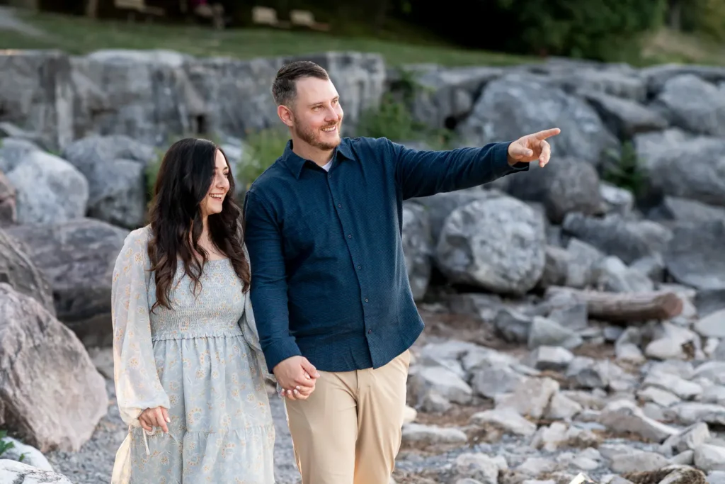a man points something out to his partner as they walk along a rocky beach in Queen's Royal Park. Part of an engagement shoot Shot in Niagara-on-the-lake by Pixelesque Photography.