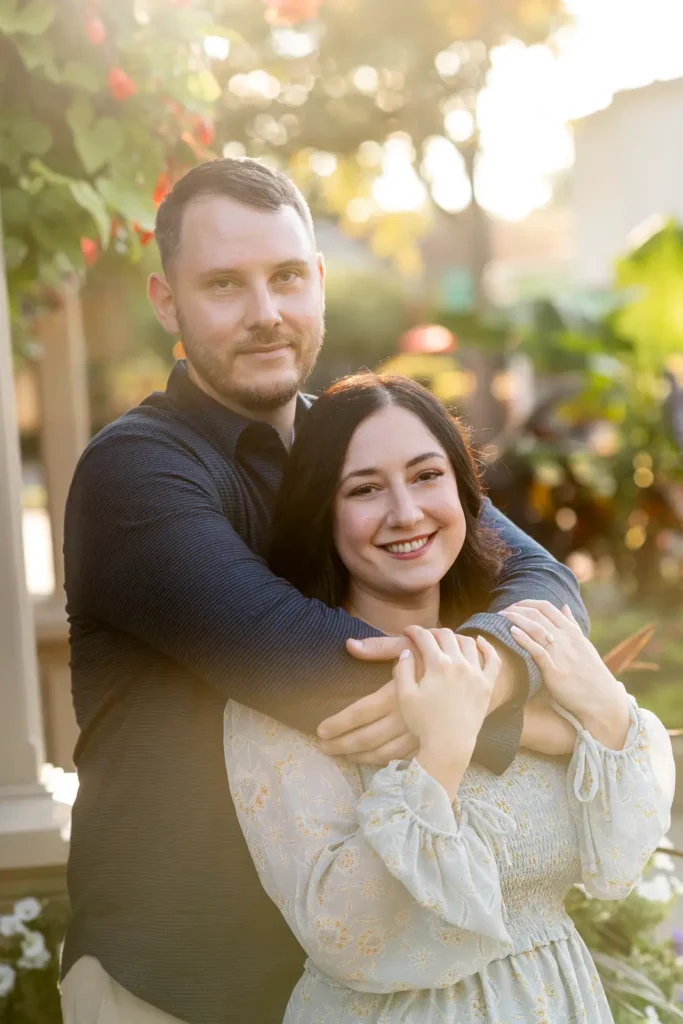 A man embraces his partner from behind as they both smile and the sun flares from behind them. Shot in Niagara-on-the-lake by Pixelesque Photography.