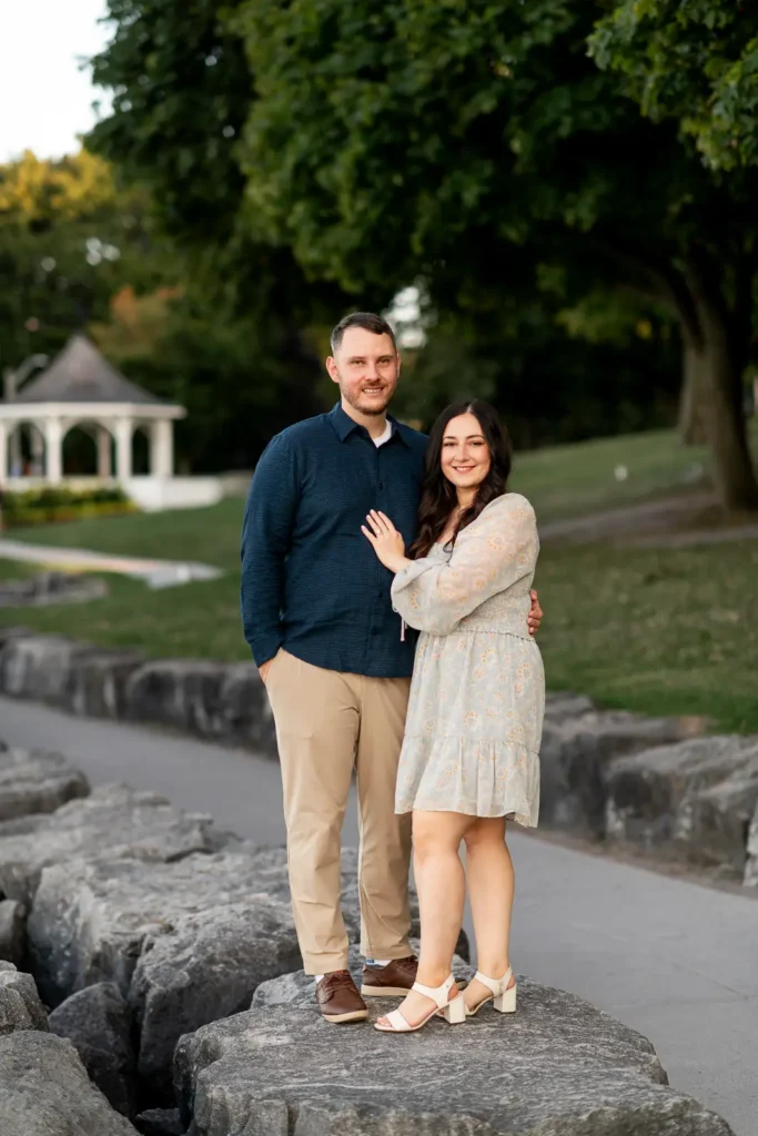 a couple stands on some rocks with the iconic queen's royal park gazebo in the background.