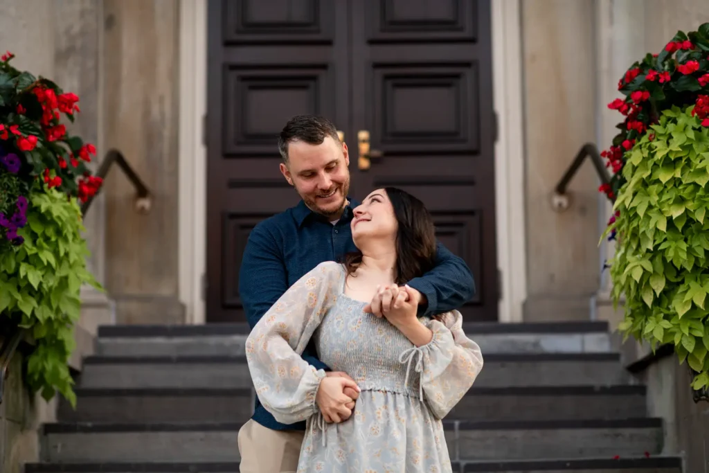 a couple pose and embrace in front of the NOTL courthouse. Part of an engagement shoot Shot in Niagara-on-the-lake by Pixelesque Photography.