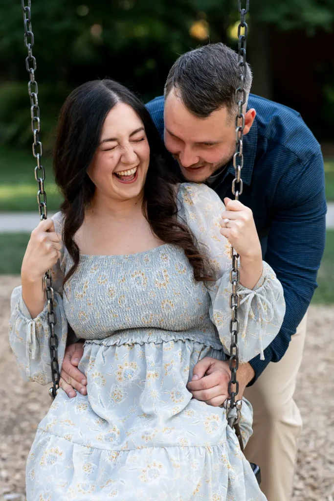 a man laughs as he pushes his partner on a swing at Simcoe park. Shot in Niagara-on-the-lake by Pixelesque Photography.