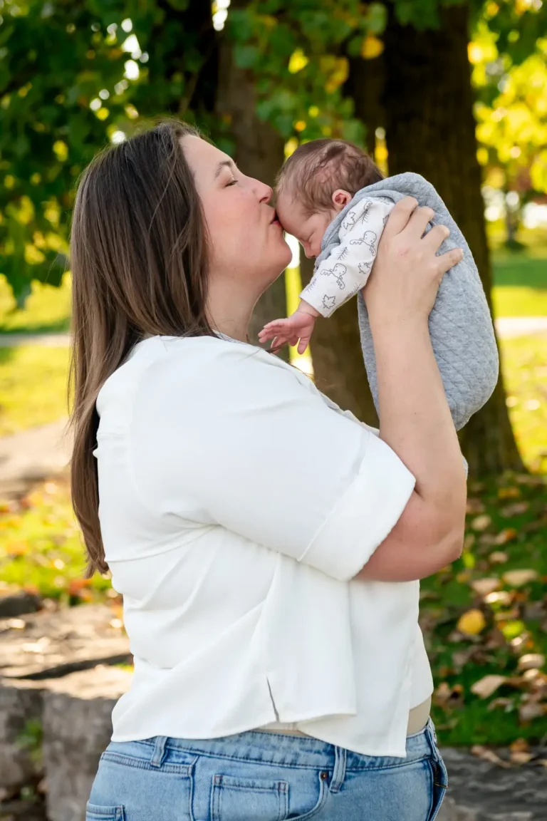 a mother kisses her newborn baby on the forehead as she holds him up in front of her. Shot at bayfront park by Pixelesque photography - Hamilton Family Photographer