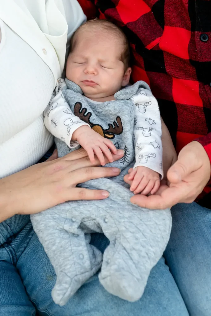 a newborn baby sleeps between their parents while they hold their hands. Shot at bayfront park by Pixelesque photography - Hamilton Family Photographer