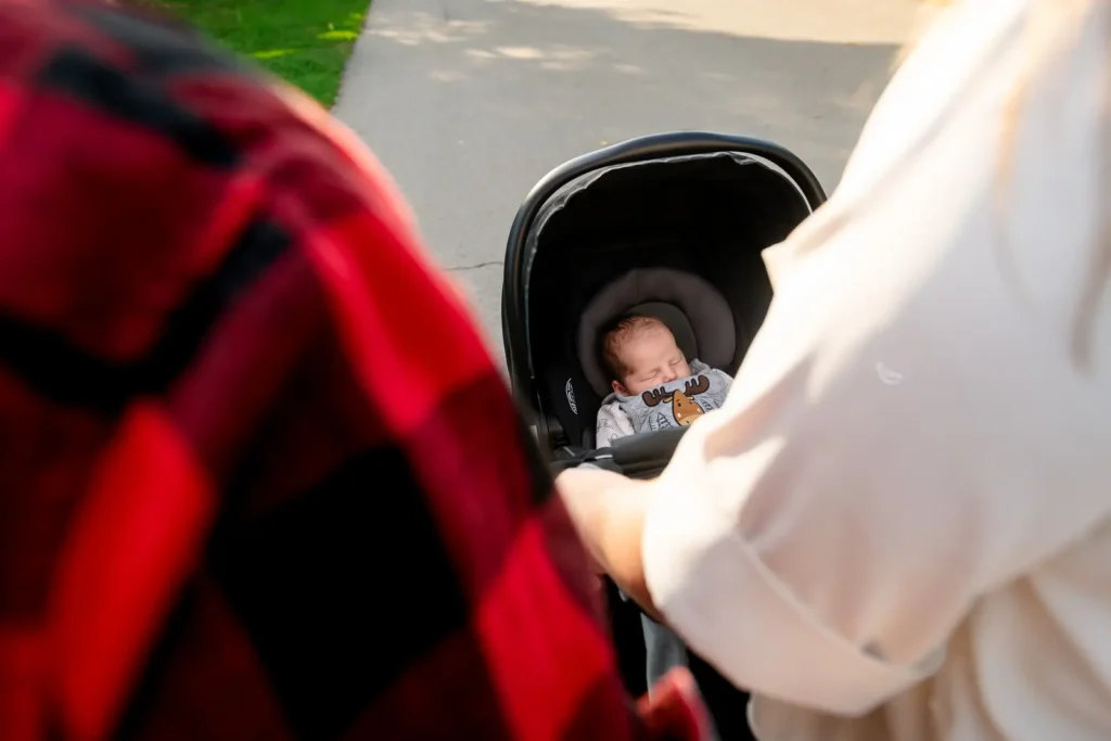 a newborn baby sleeps in their stroller as seen between the parents from behind. Shot at bayfront park by Pixelesque photography - Hamilton Family Photographer