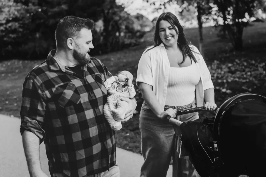 a black and white image of a father holding his newborn as the mother pushes the stroller beside them. Shot at bayfront park by Pixelesque photography - Hamilton Family Photographer