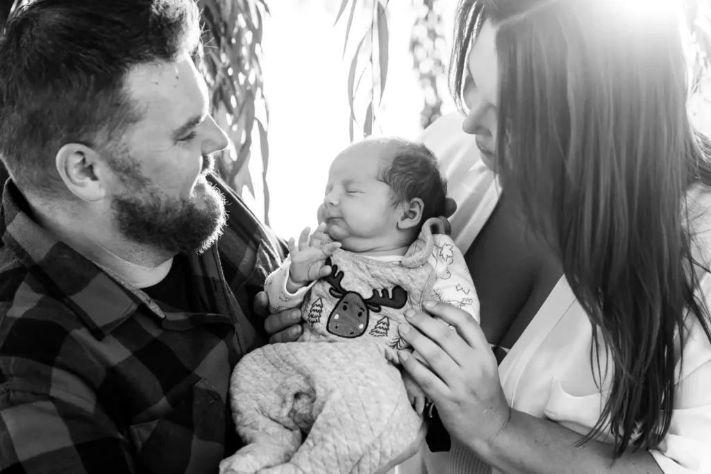 a black and white picture of a couple holding their sleeping newborn up between them and looking at him. Shot at bayfront park by Pixelesque photography - Hamilton Family Photographer