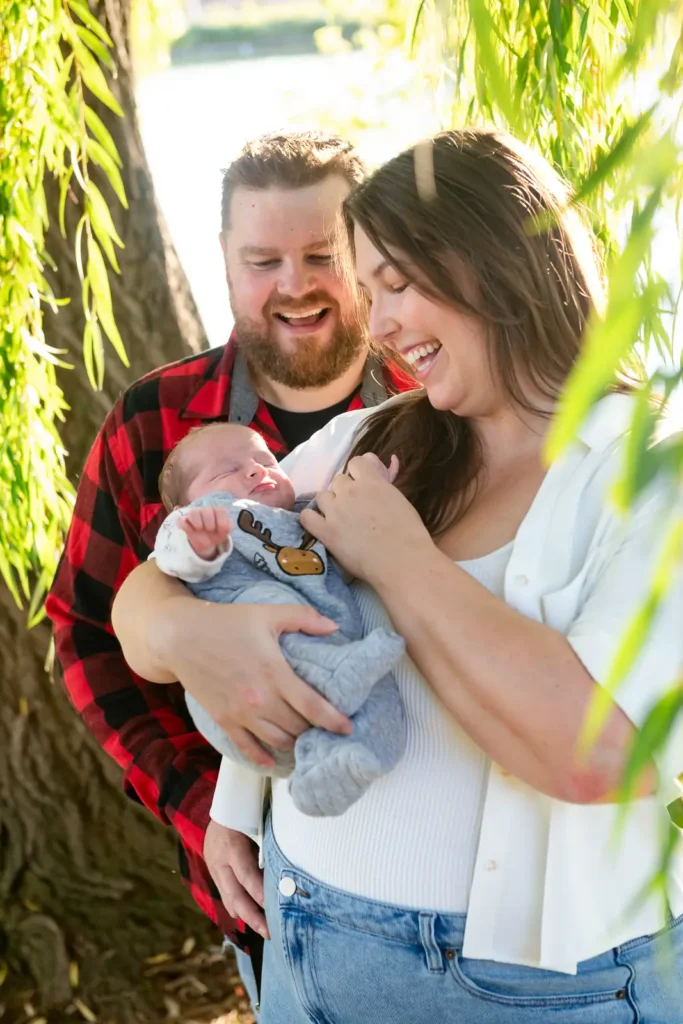 a mother holds her newborn up to her chest and the father laughs behind them. Shot at bayfront park by Pixelesque photography - Hamilton Family Photographer