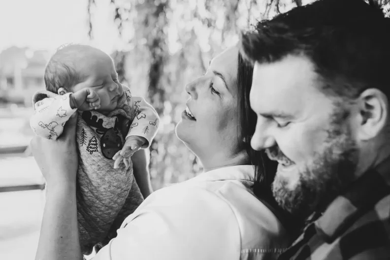 a woman holds her newborn up and the father is beside them. Shot at bayfront park by Pixelesque photography - Hamilton Family Photographer