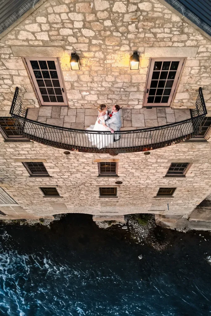 A couple have a quiet moment on the terrace of Cambridge Mill as the river flows beneath them. A wedding day drone photograph shot by Pixelesque Photography - Hamilton wedding Photographer.