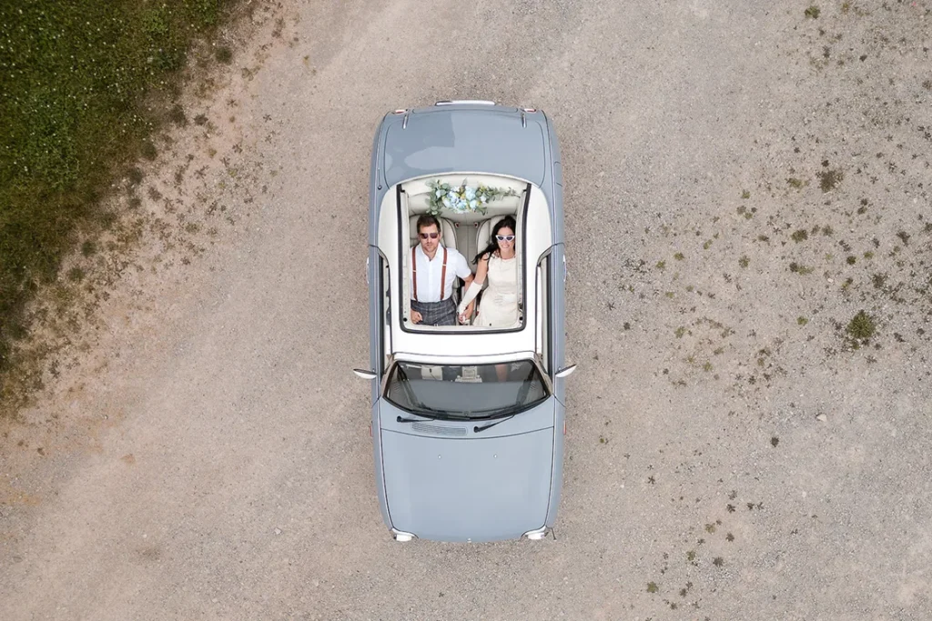 A retro styled couple hold hands while sitting back in their retro car and look up at the dron through the open sunroof. An engagement session drone photograph shot by Pixelesque Photography - Hamilton wedding Photographer.