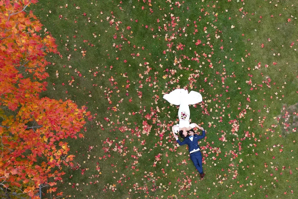 A couple lay amongst fallen autumn leaves in Bayfront Park. A wedding day drone photograph shot by Pixelesque Photography - Hamilton wedding Photographer.