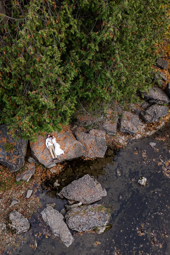 A couple lay together on a rock beside the river at Elora Gorge. An engagement session drone photograph shot by Pixelesque Photography - Hamilton wedding Photographer.