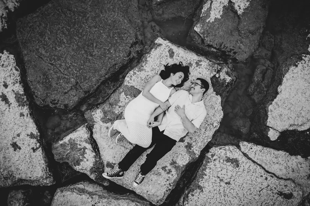 A couple lay beside each other amidst a mosaic of rocks at Scarborough Bluffs Park. A wedding day drone photograph shot by Pixelesque Photography - Hamilton wedding Photographer.