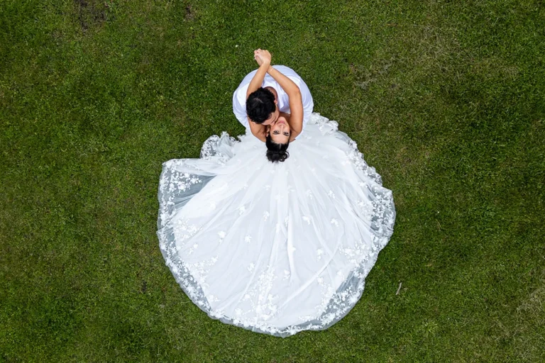 a bride and groom share an embrace as she looks up at the camera and the details of her flowing wedding dress are shown off. A wedding day drone photograph shot by Pixelesque Photography - Hamilton wedding Photographer.